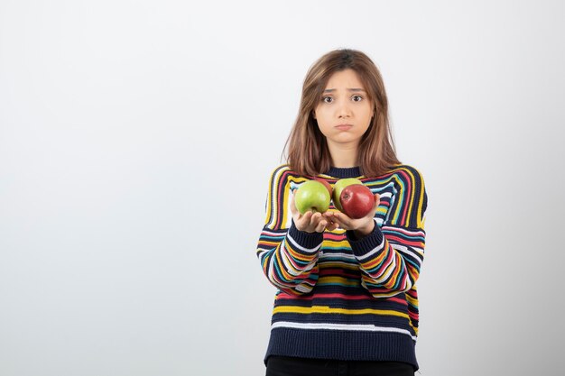 Adorable young girl in casual clothes holding colorful apples.