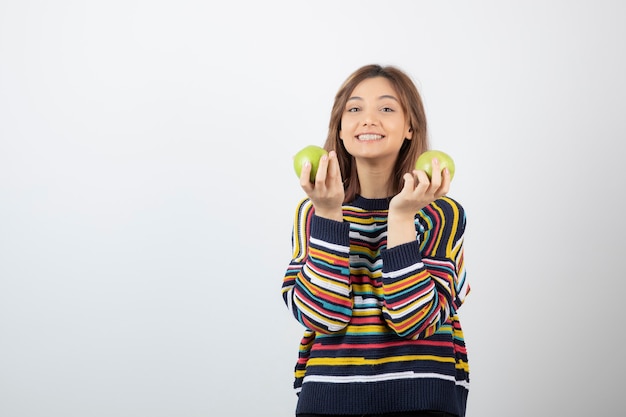Adorable young girl in casual clothes holding green apples on white.