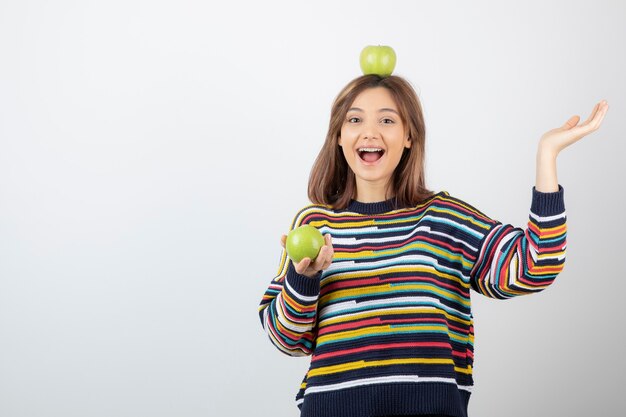 Adorable young girl in casual clothes looking at green apples on white.