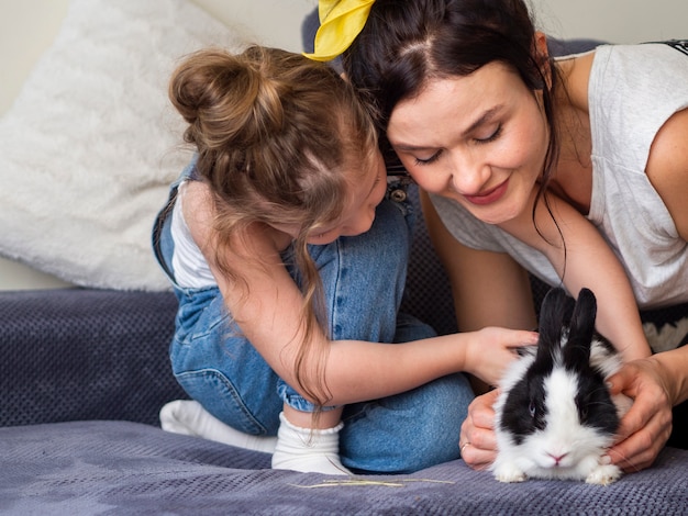Adorable young girl and mother playing with rabbit