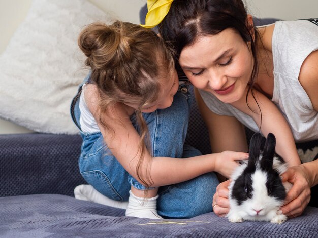 Очаровательная молодая девушка и мать играют с кроликом