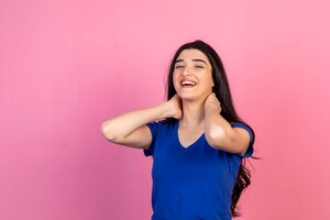 Adorable young girl putting her hands to her neck and laughing on pink background high quality photo