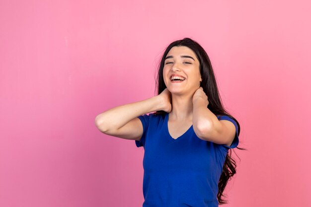 Adorable young girl putting her hands to her neck and laughing on pink background High quality photo