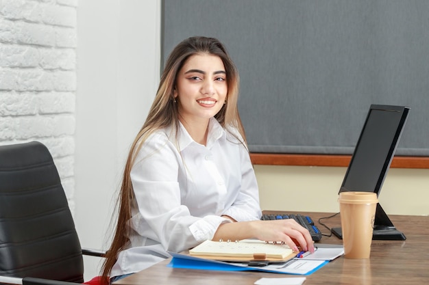 Foto gratuita adorabile ragazza seduta dietro la scrivania e sorridente