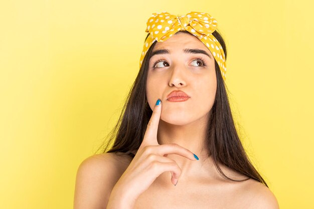 Adorable young girl standing on yellow background and thinking