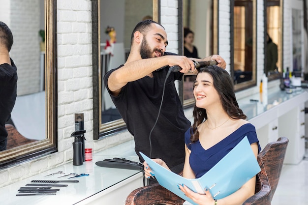 Adorable young lady smiling and barber using hair dryer on her hair High quality photo