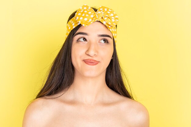 Adorable young lady standing on yellow background and looking up