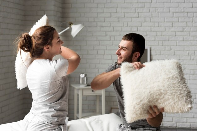 Adorable young man and woman pillow fighting