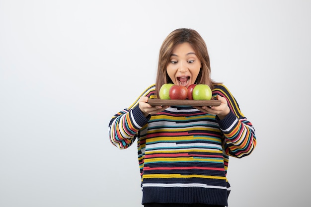 Adorable young woman in casual clothes eating bunch of apples.