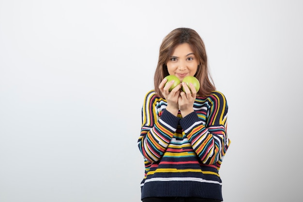 Adorable young woman in casual clothes holding green apples on white background. 