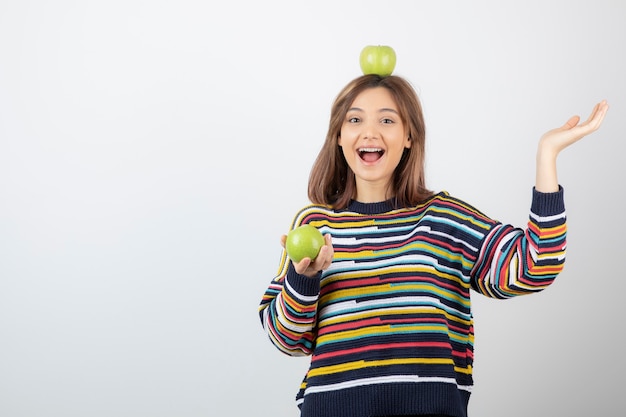 Adorabile giovane donna in abiti casual guardando le mele verdi su sfondo bianco.