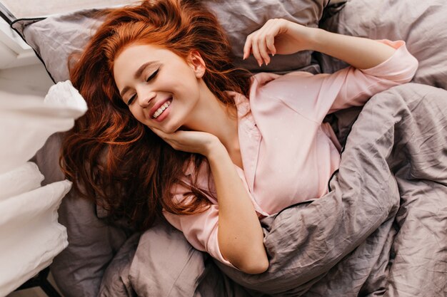 Adorable young woman spending morning in bed. Graceful ginger girl relaxing in weekend.
