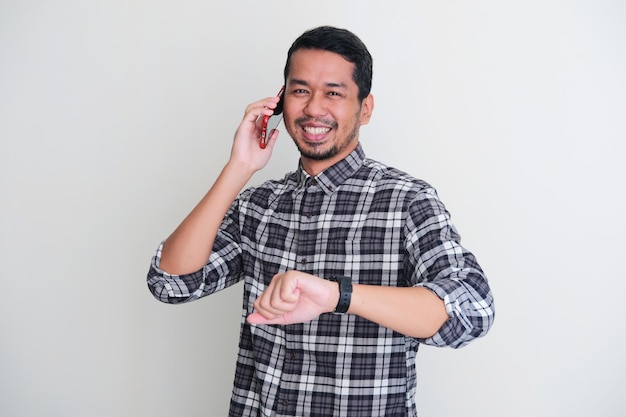 전화를 걸고 시계를 보여주는 동안 카메라에 미소 짓는 성인 아시아 남자 프리미엄 사진