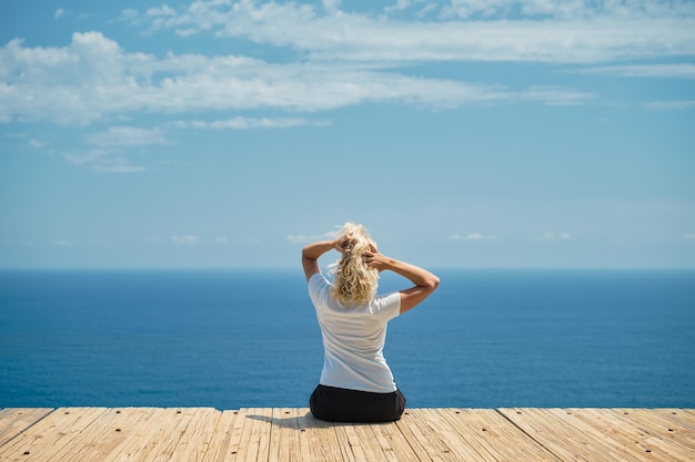 Adult beautiful woman rejoices in a warm day blonde sits against the backdrop of a magnificent seascape a journey through the Greek islands a famous place for vacation and travel