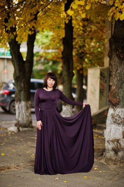 Adult brunette woman at violet gown on autumn fall background