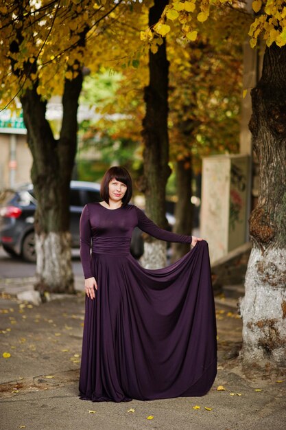 秋の秋の背景に紫のガウンで大人のブルネットの女性
