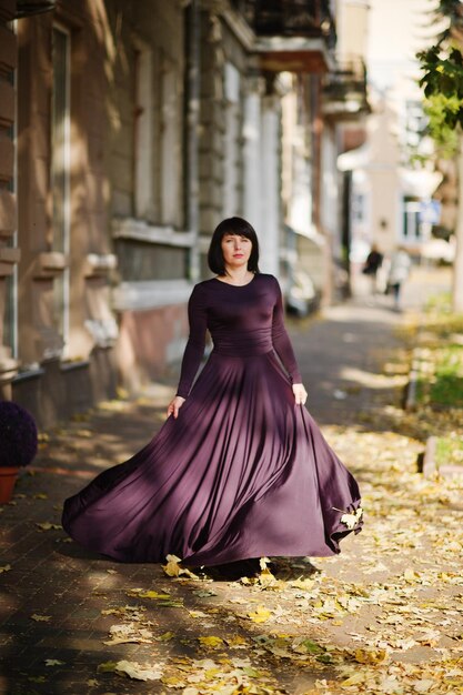 Adult brunette woman at violet gown on autumn fall background