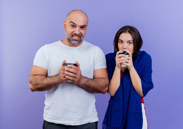 Adult couple impressed woman wrapped in shawl smiling man both holding plastic cup of coffee looking 