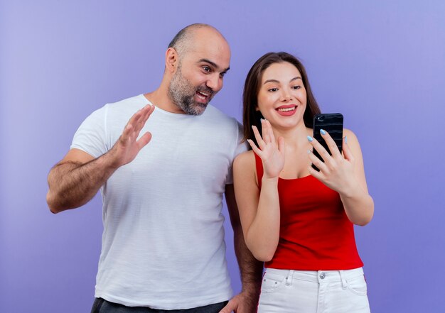 Adult couple smiling woman holding mobile phone impressed man both looking and waving at phone 