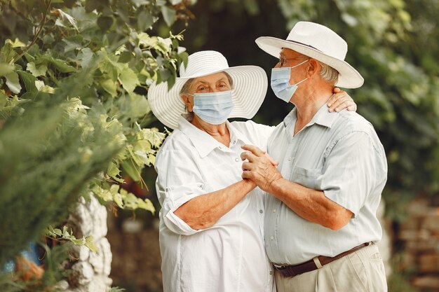 Adult couple in a summer garden. Coromavirus theme. People in a medical mask. Handsome senior in a white shirt.