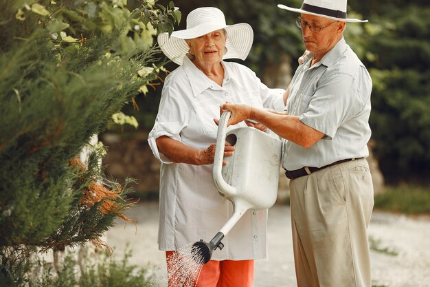 サマーガーデンの大人のカップル。白いシャツを着たハンサムな先輩。帽子をかぶった女性。家族の水やり。