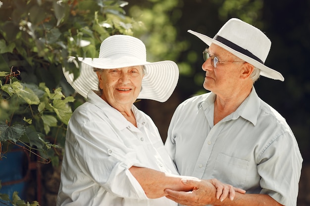 Adult couple in a summer garden. Handsome senior in a white shirt. Woman in a hat.