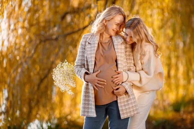 Adult daughter hugs her pregnant mom on a sunny autumn day in nature