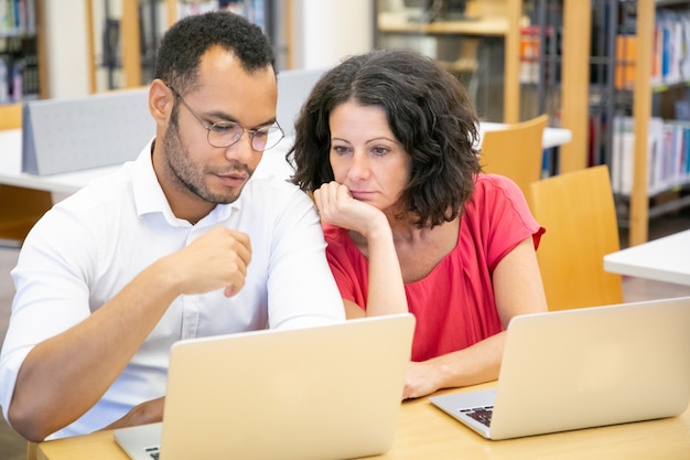 Adult female student consulting monitor of college mate