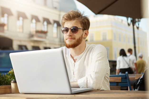 Adult ginger handsome man with laptop computer sitting on the terrace of a restaurant or cafe