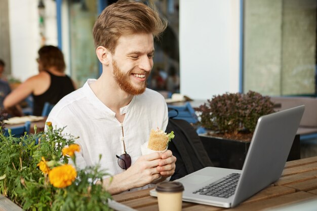 Adult ginger handsome man with laptop computer sitting on the terrace of a restaurant or cafe