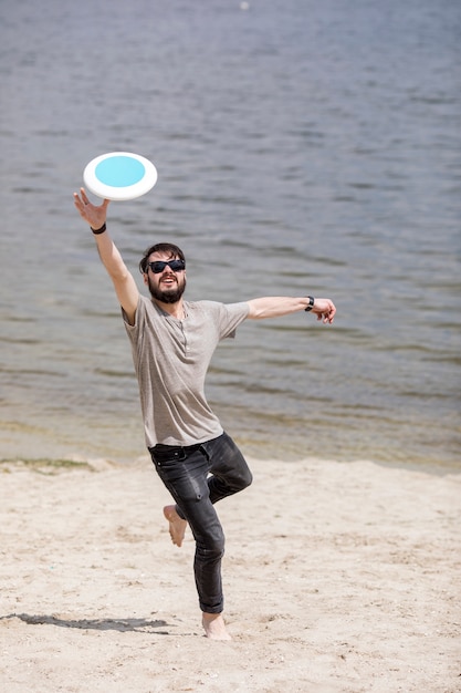 Foto gratuita funzionamento del maschio adulto e frisbee di cattura sulla spiaggia