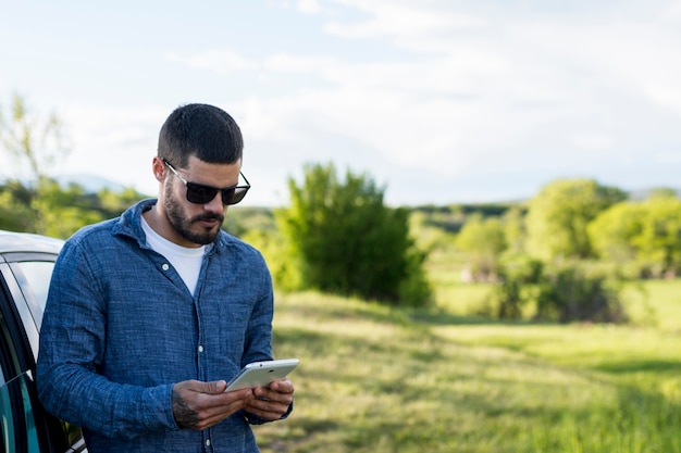 Adult man leaning on car and using tablet