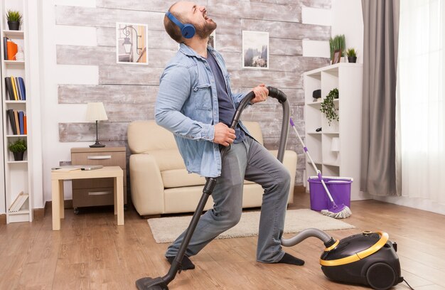 Взрослый мужчина слушает рок-музыку в наушниках во время уборки дома