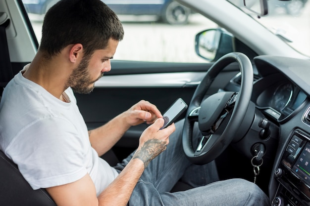 Adult man sitting in car and using smartphone