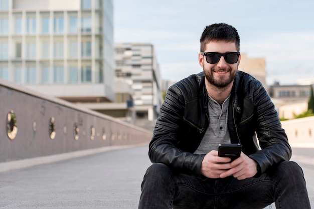 Free photo adult man sitting on ground holding smartphone