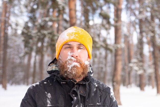 An adult man with a beard in a winter forest all face in the snow, frozen, unhappy with the cold