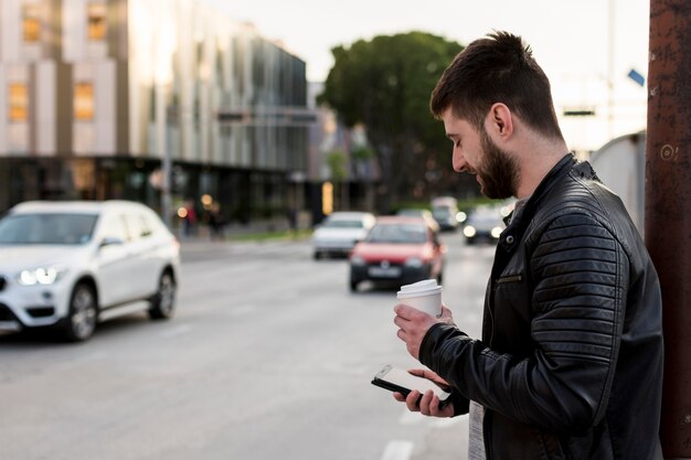 携帯電話を使用してコーヒーを持つ成人男性