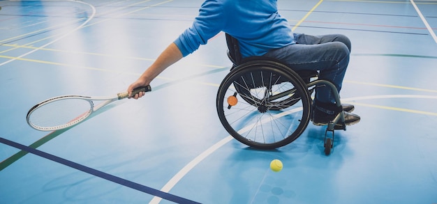Adult man with a physical disability who uses wheelchair playing tennis on indoor tennis court