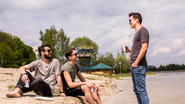 Adult men sitting on beach and listening to friend 