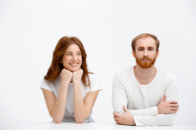 Adult redhead man and woman sit at desk like classmates