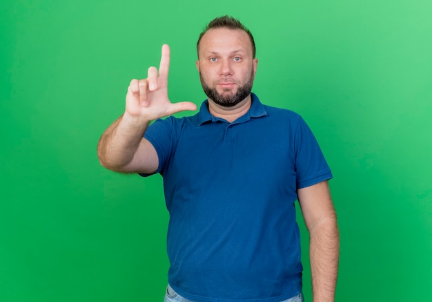 Взрослый славянский мужчина смотрит, делая жест неудачника, изолированного на зеленой стене
