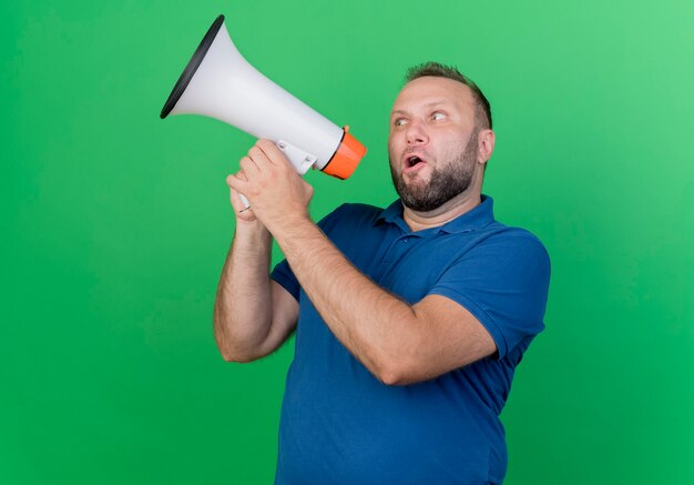 Adult slavic man looking at side talking by speaker isolated on green wall