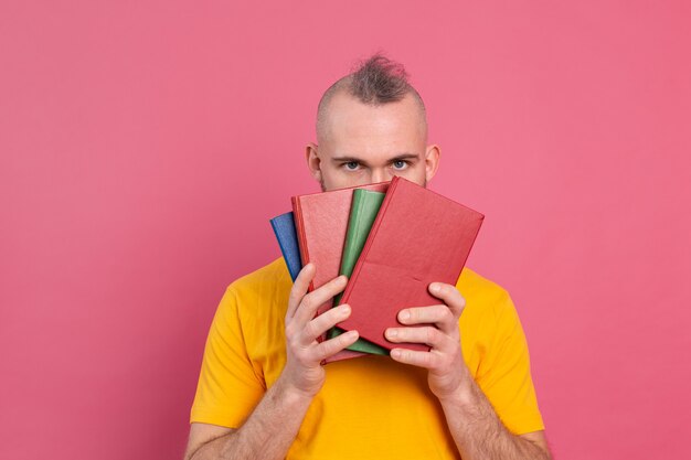 大人の笑顔のカジュアルな服の男は、ピンクで隔離された自分自身にお気に入りの本を抱きしめます