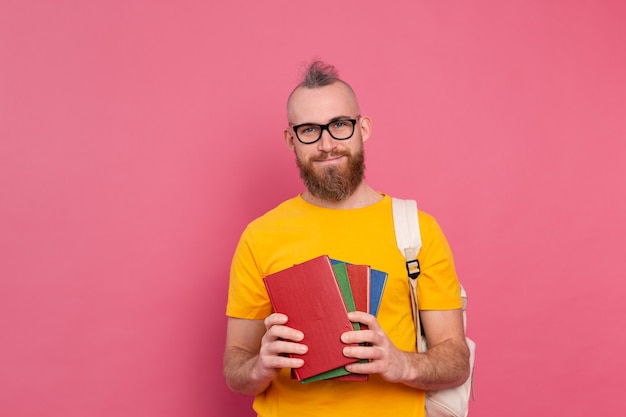 Adult student cheerful casual wear guy with beard and backpack holding books isolated on pink