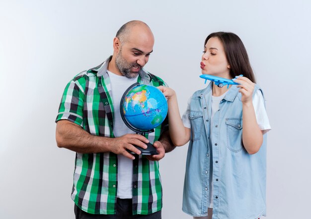 大人の旅行者のカップルは、地球儀を持っている男性と、地球儀に触れて地球儀を見ている模型飛行機を持っている女性に感銘を与えました