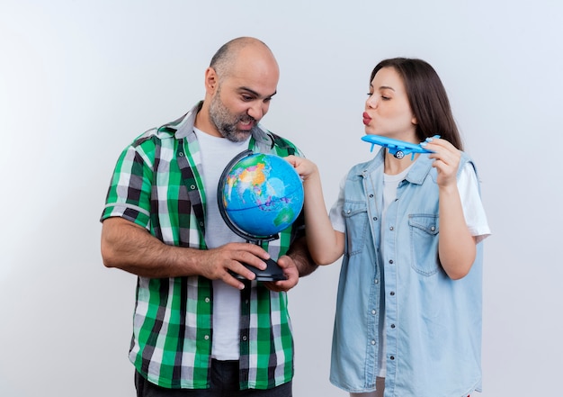 Adult traveler couple impressed man holding globe and woman holding model plane touching globe and both looking at globe 