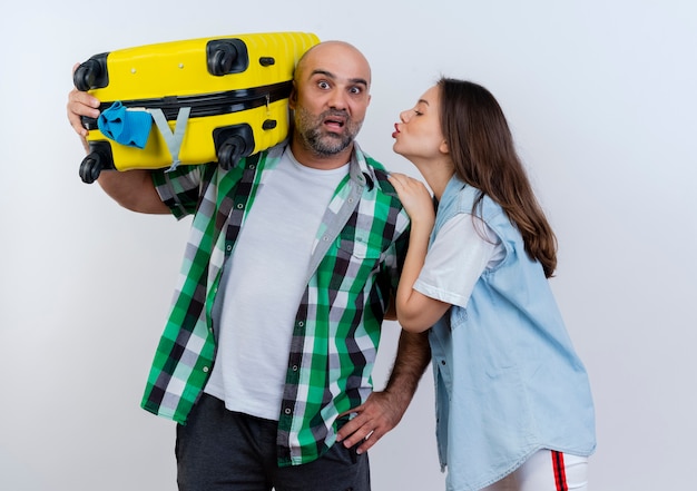 Free photo adult traveler couple impressed man holding suitcase on shoulder looking keeping hand on waist woman touching his shoulder looking at him and doing kiss gesture