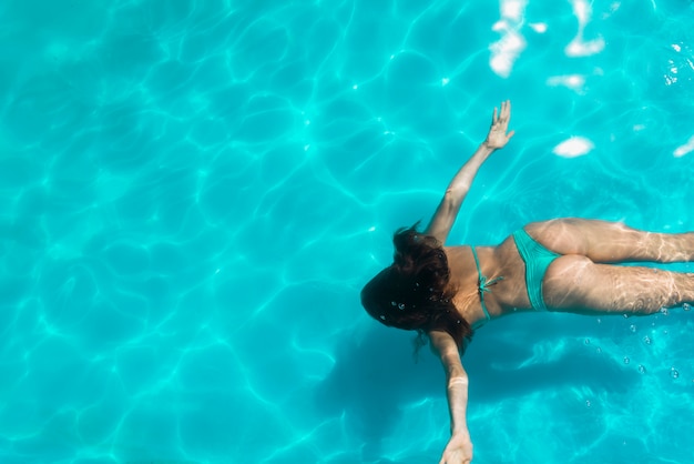 Adult woman floating under bright pool water