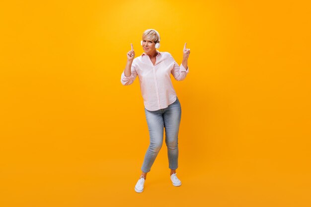 Adult woman in headphones pointing up on orange background
