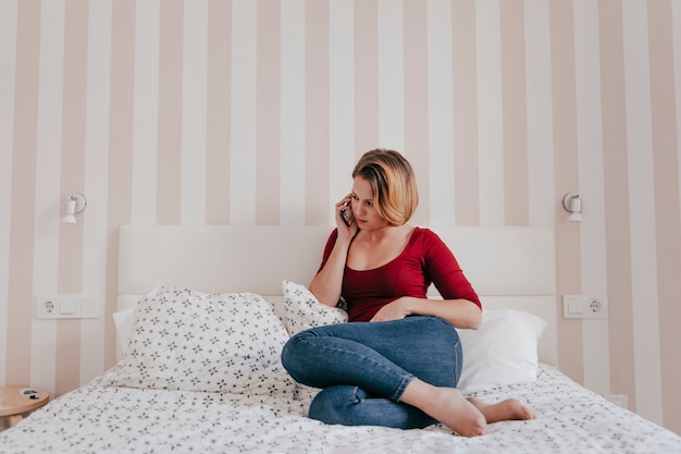 Free photo adult woman speaking on smartphone on bed